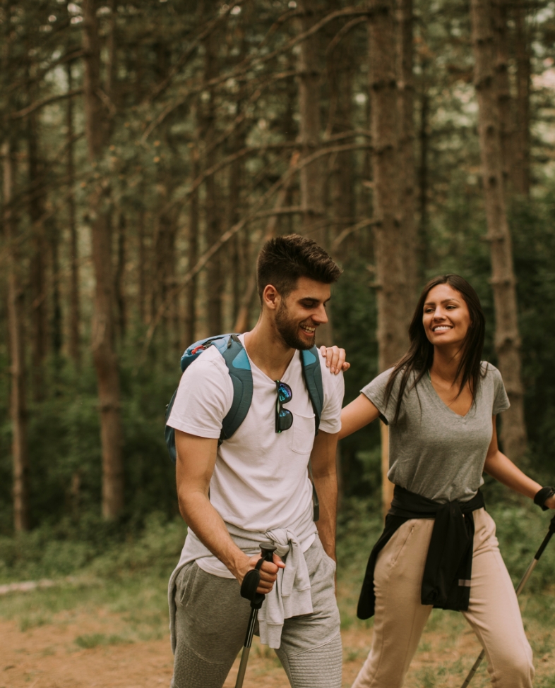 Two people hike through the woods while laughing.