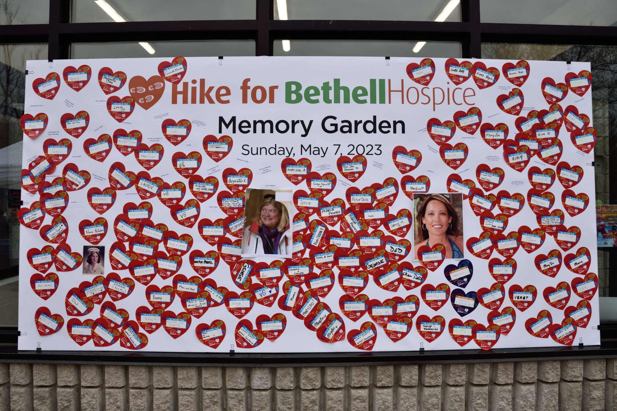 large poster on the windows of a store front with small hearts covering it and the words Hike for Bethell Hospice Memory Garden
