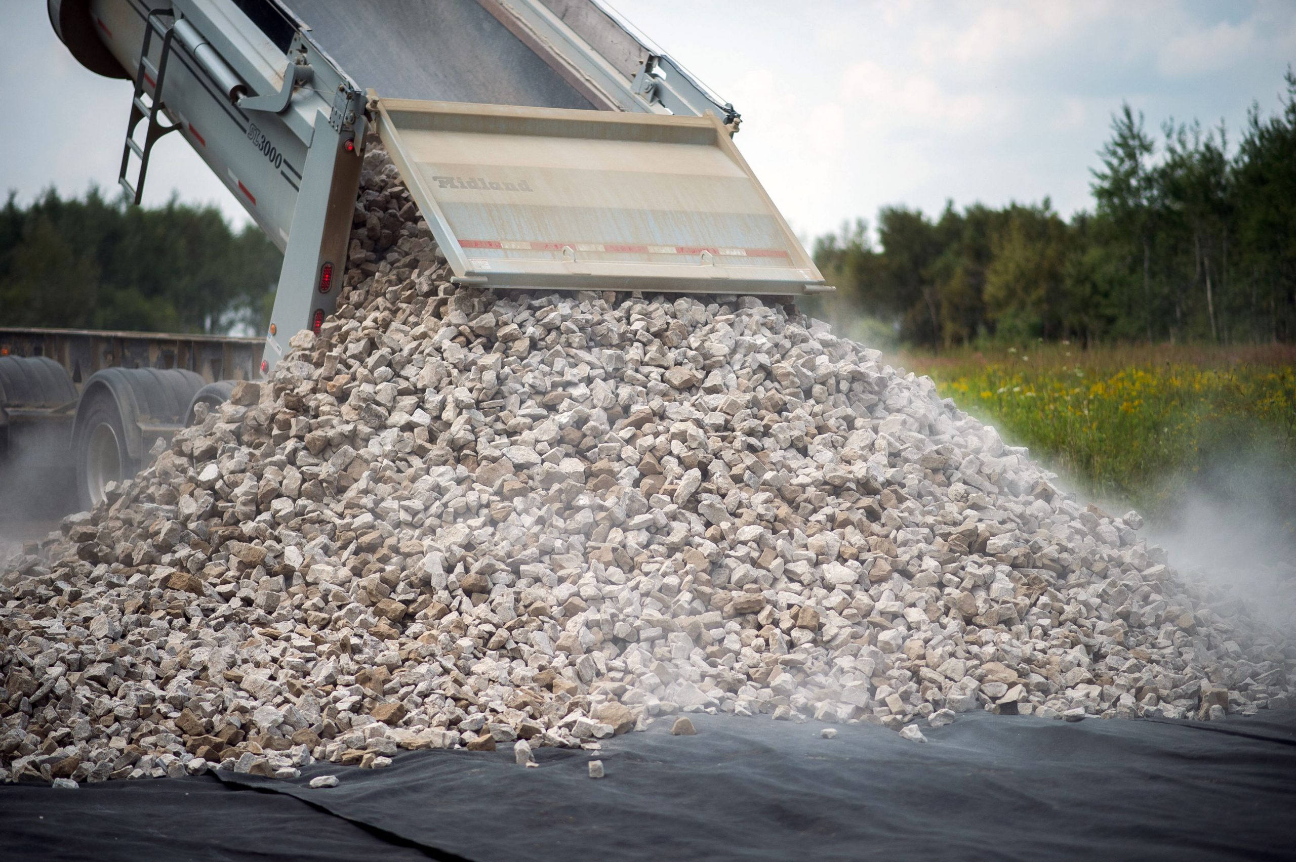 A dump truck unloading stones onto a tarp.