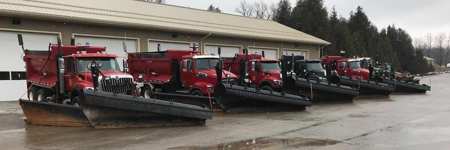 A row of parked snowplows in front of a garage.