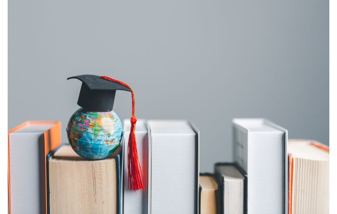 A small globe with a graduation hat sits on top of a collection of hardcover novels