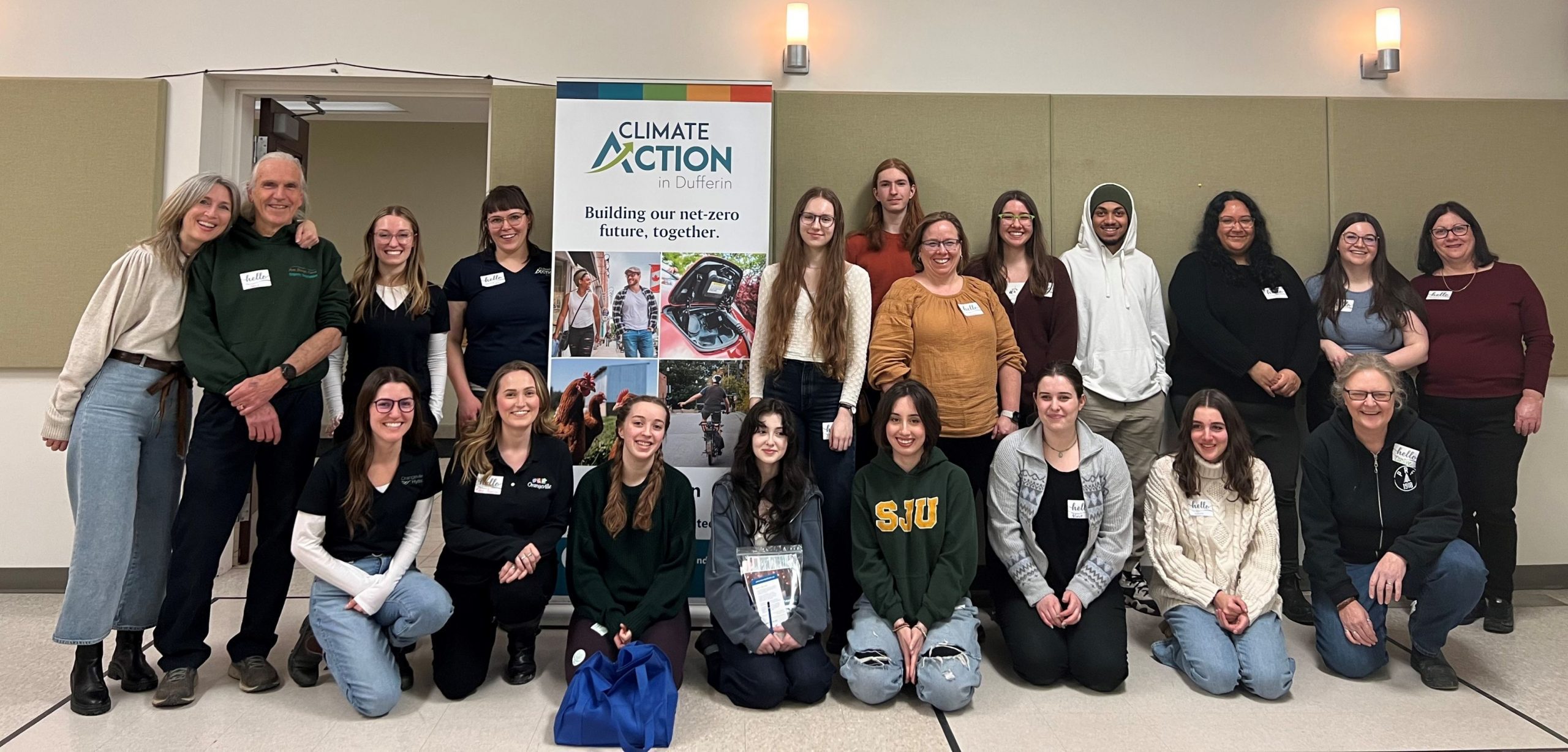 large group of people posing for a photo around a banner