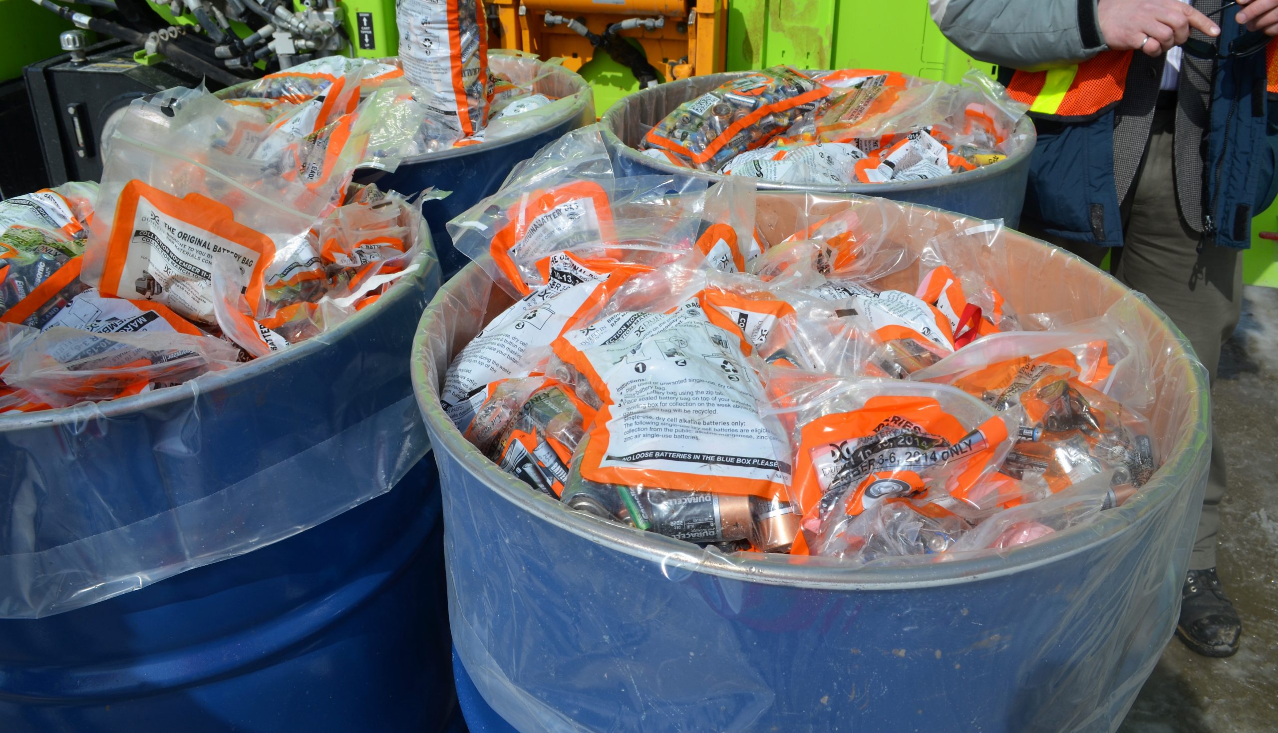 four large blue steel drums filled with plastic bags of used batteries