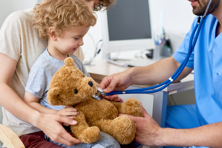 A child has his teddy bear examined by a physician.