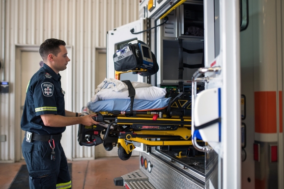 Paramedic loading empty stretcher into the back of an ambulance