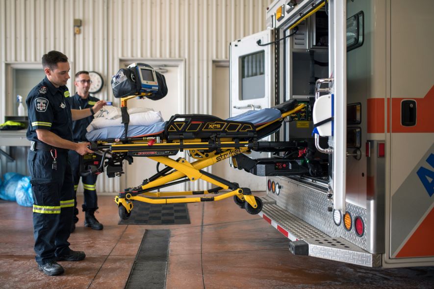 two paramedics loading empty stretcher into the back of an ambulance
