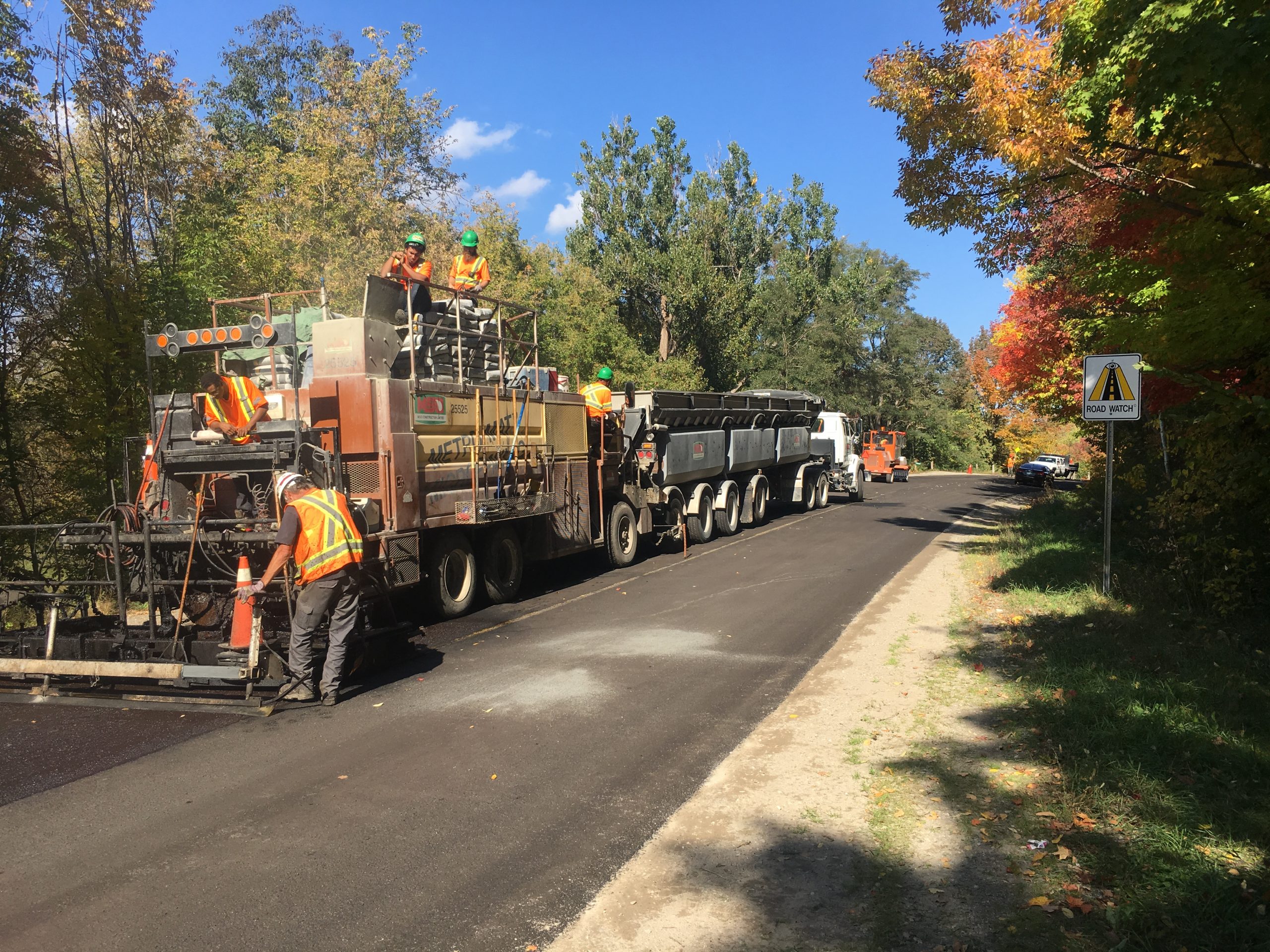 Paving equipment on a country road while workers are onsite supervising.