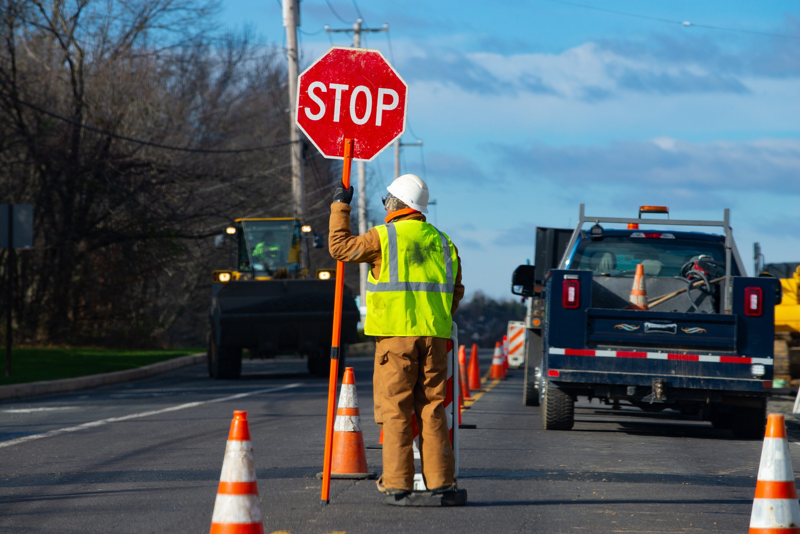 A worker is directing traffic on a road being occupied by construction vehicles