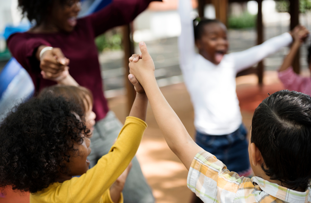 A groups of young children hold hands and laugh in a circle.