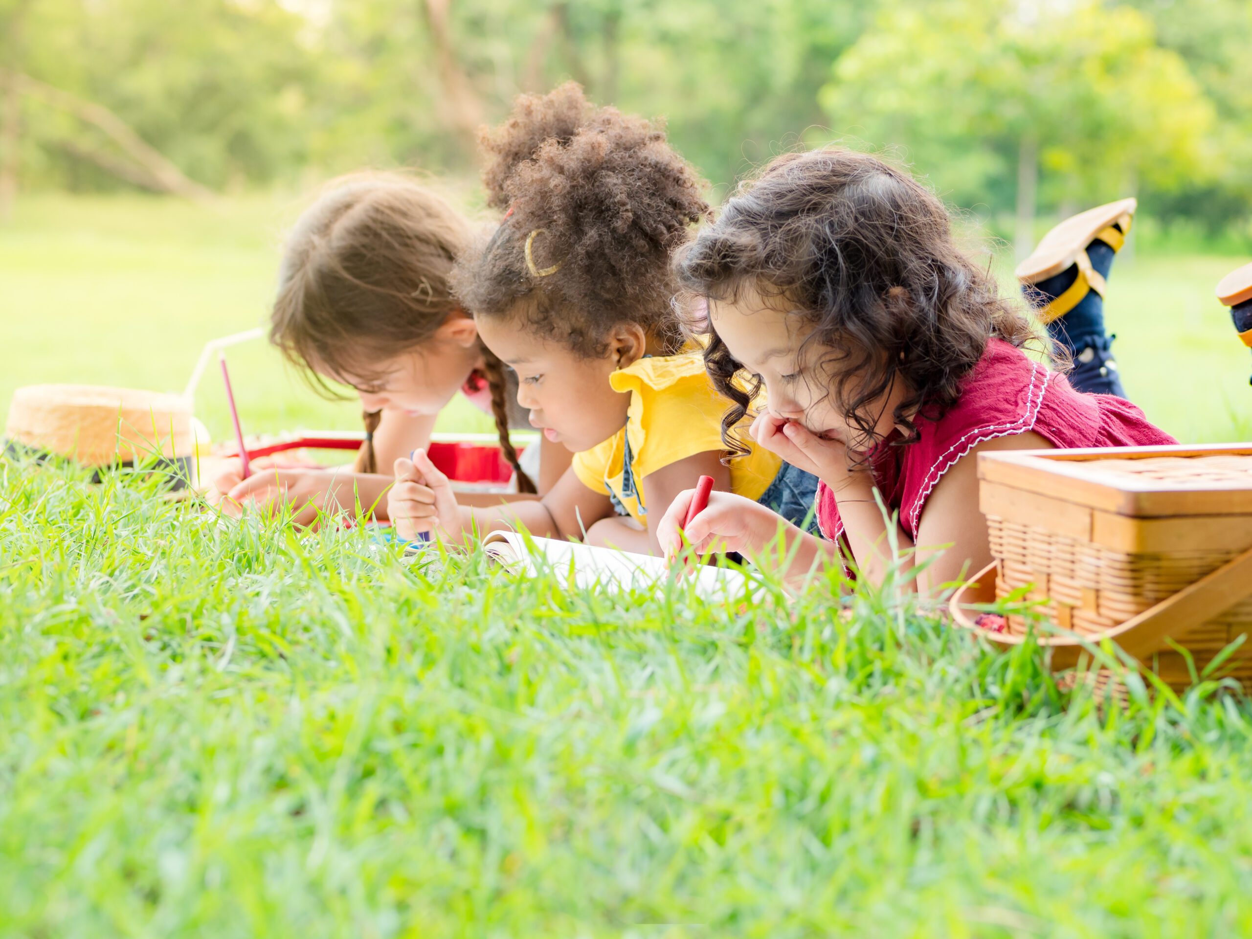 Three children lay in the grass drawing.