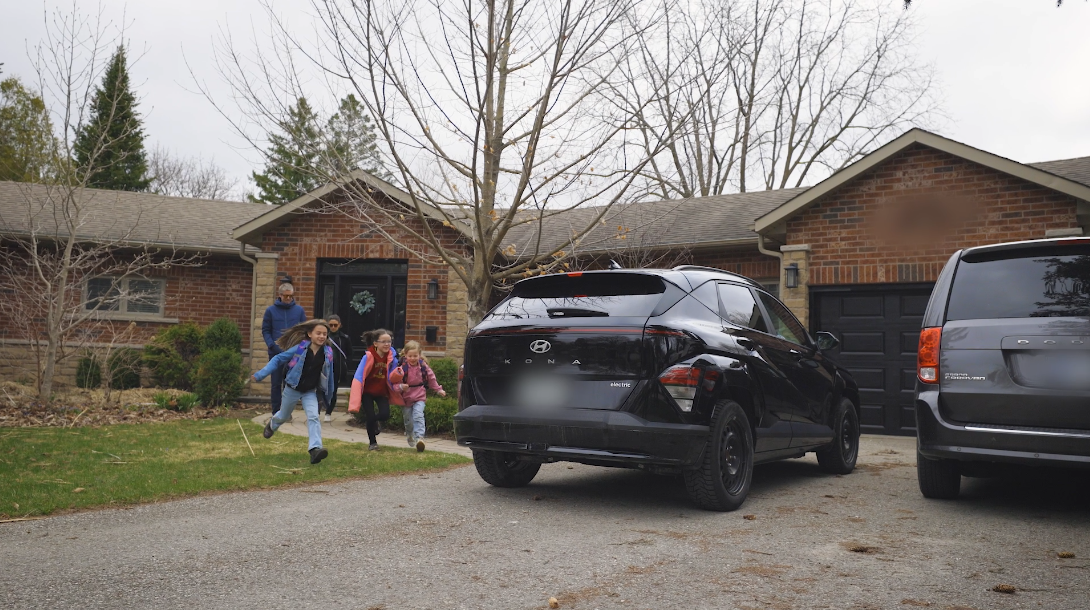 A family with three children run from the front door of home to black electric SUV